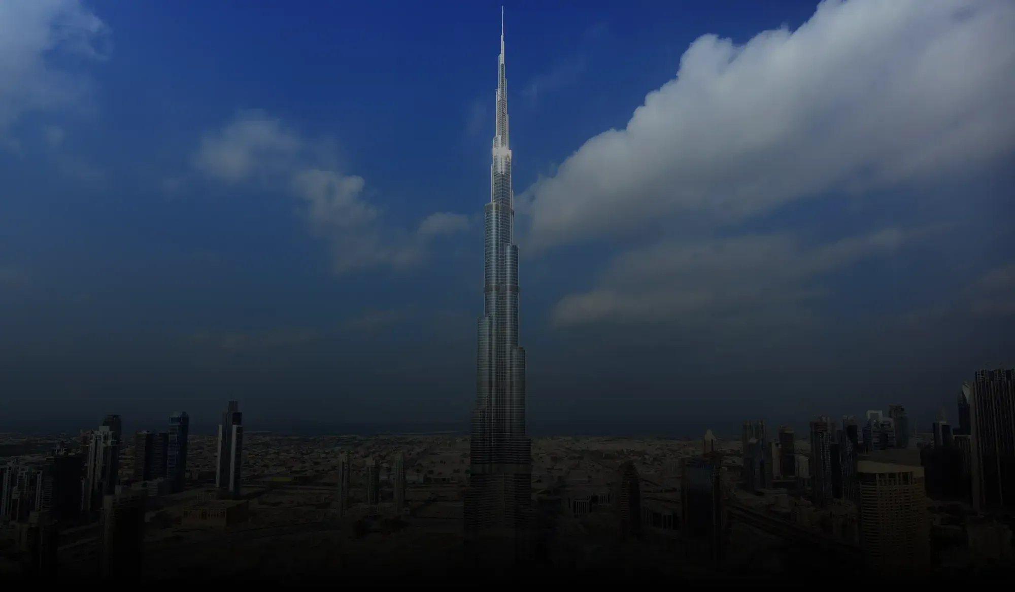 Burj Khalifa towering above Dubai cityscape under a blue sky with scattered clouds.