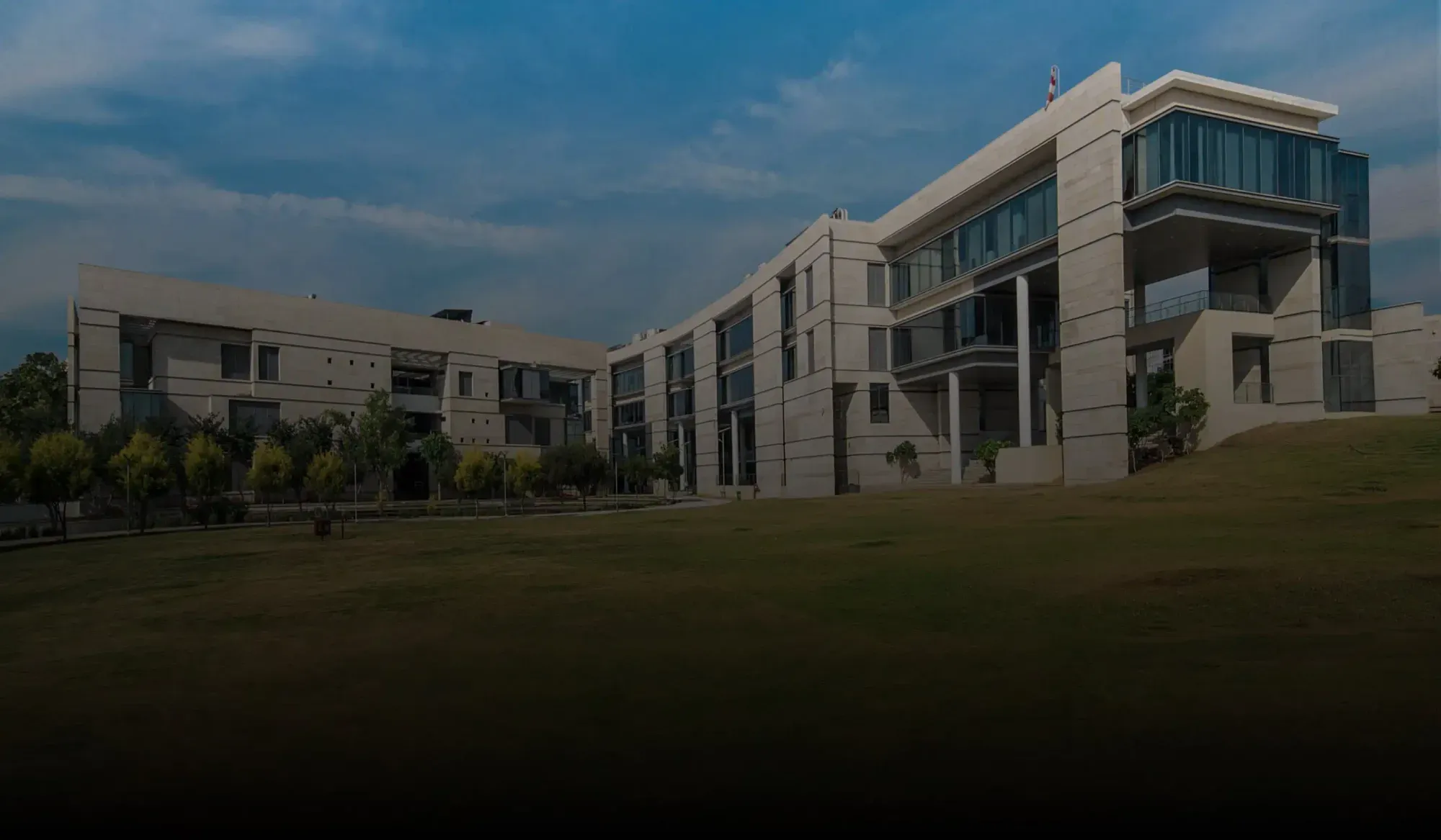 Modern campus buildings with large windows and a green lawn under a blue sky.