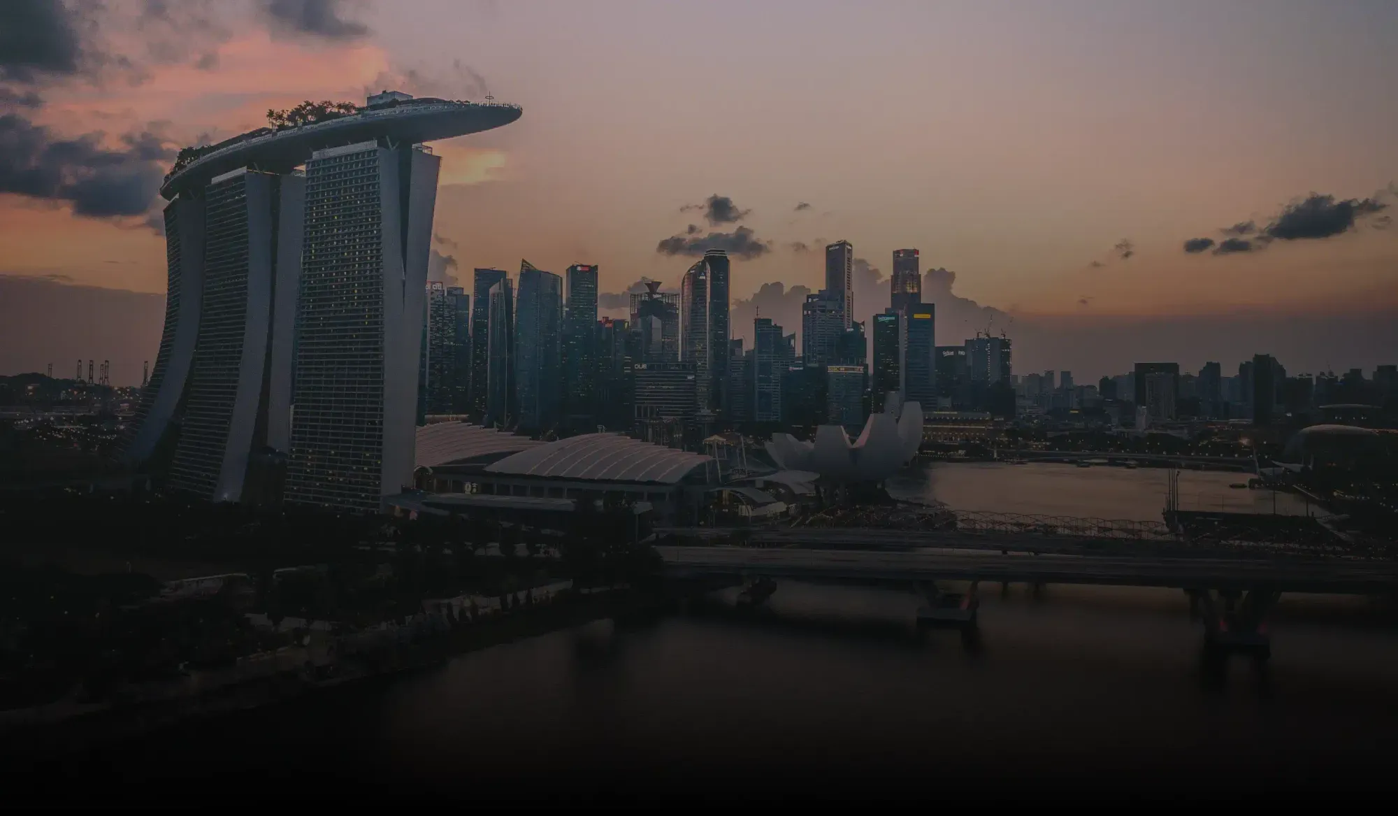 Singapore skyline at dusk featuring Marina Bay Sands hotel with illuminated skyscrapers and waterfront.