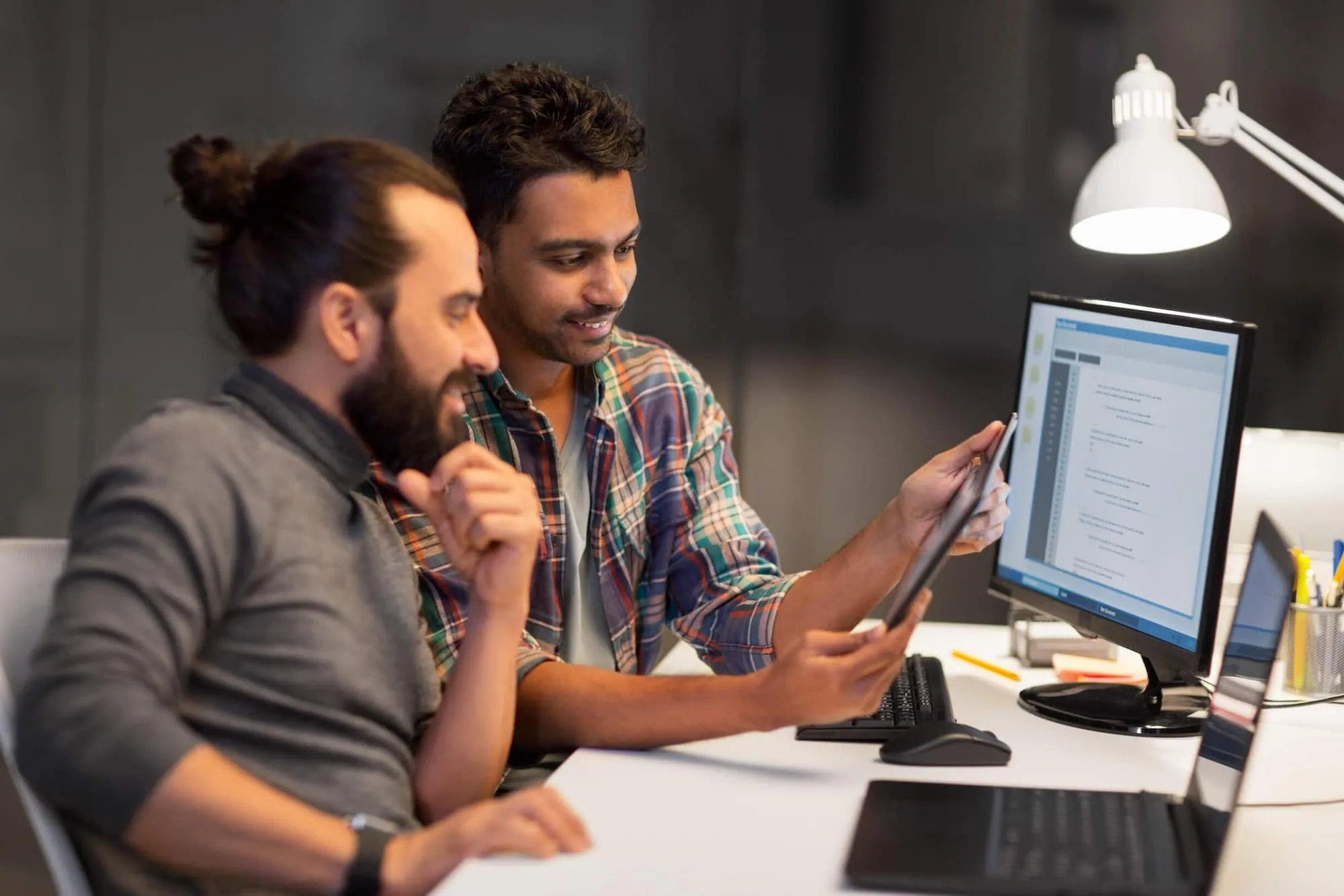 Three young professionals reviewing documents and working on digital devices in a modern office.
