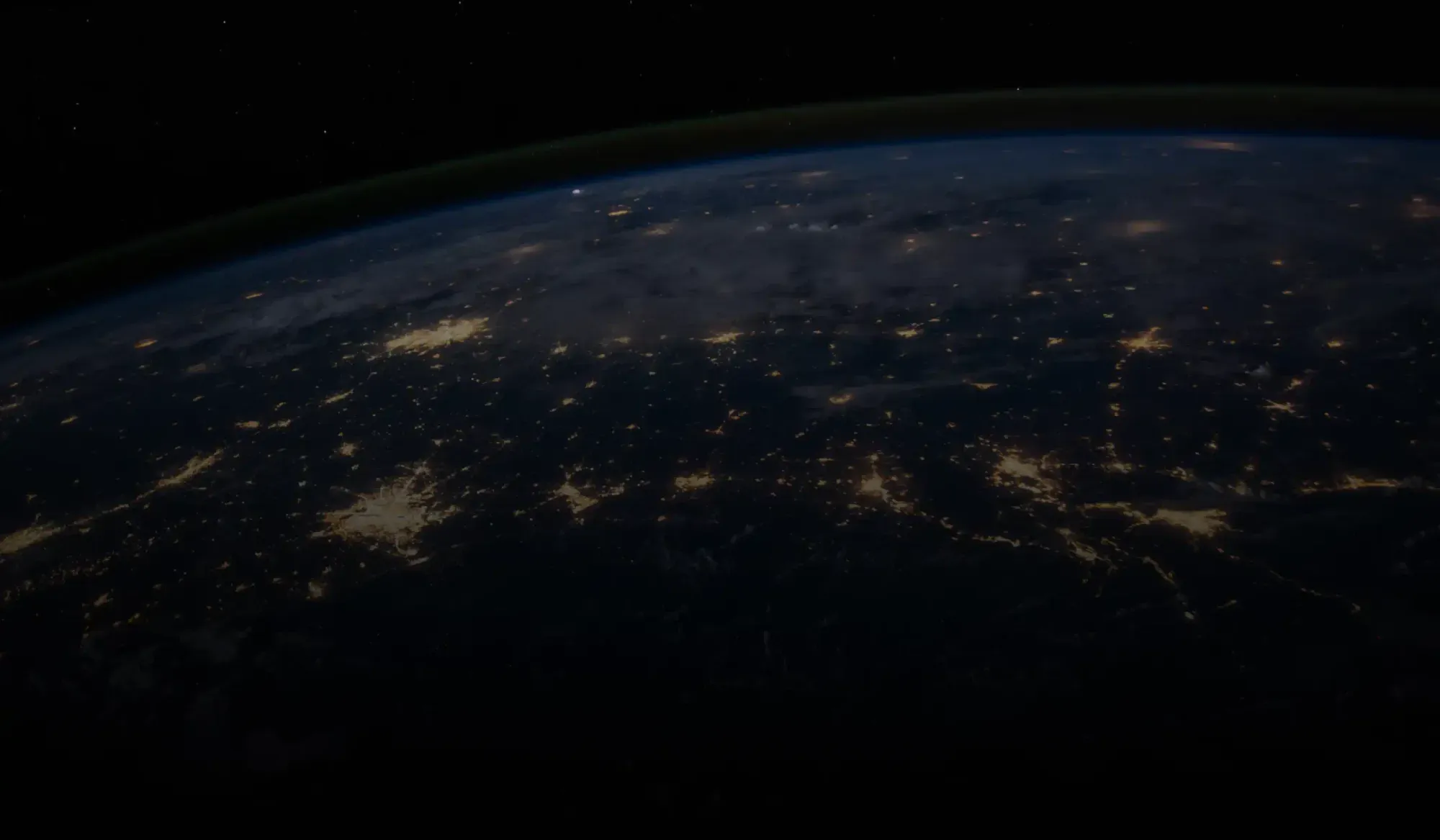 View of Earth at night from space showing illuminated city lights across a darkened landscape.