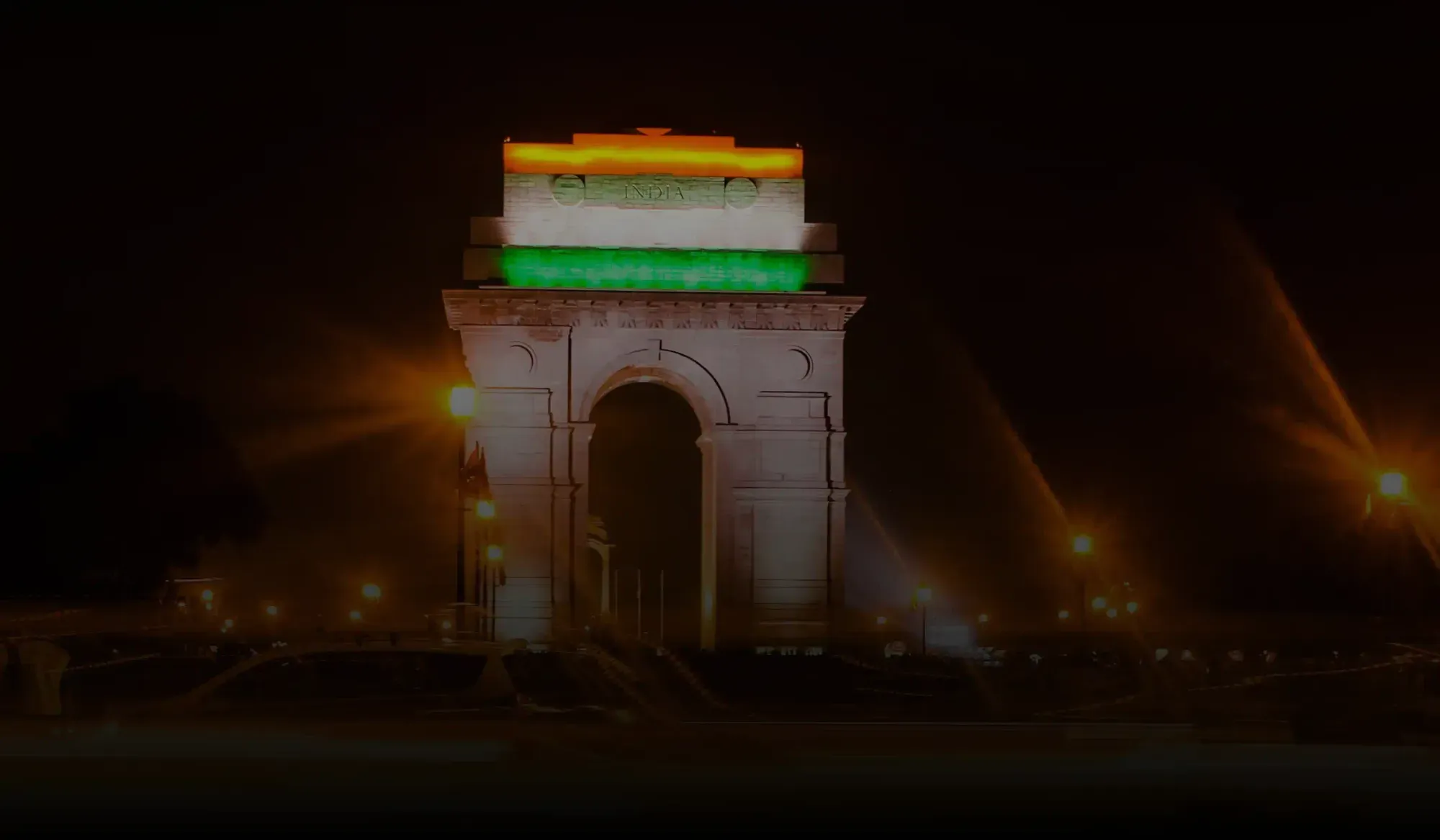 India Gate monument lit at night with the top illuminated in the colors of the Indian flag.