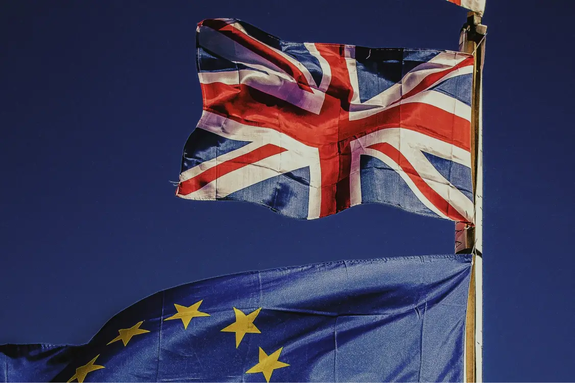 Union Jack and European Union flags waving on a flagpole against a clear blue sky.